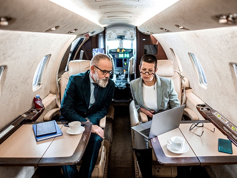 Two senior business people using Wi-Fi aboard a private jet